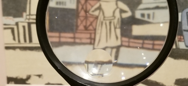 A photo of a magnifying glass held in front of a drawing of a person in a hat and trench coat facing away from the viewer. It looks like it could be a scene from an old comic book.